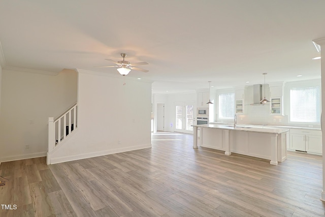 unfurnished living room featuring ceiling fan, crown molding, light wood-type flooring, and sink