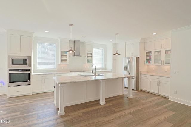 kitchen with a wealth of natural light, sink, stainless steel appliances, wall chimney range hood, and a center island with sink