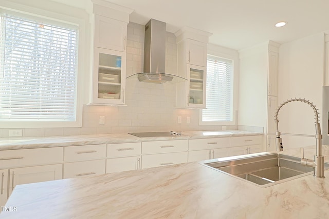 kitchen with black electric stovetop, backsplash, wall chimney exhaust hood, sink, and white cabinets