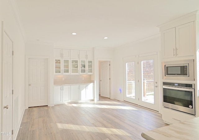 kitchen featuring decorative backsplash, appliances with stainless steel finishes, light wood-type flooring, crown molding, and white cabinetry