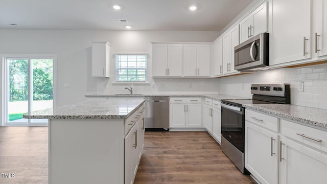 kitchen featuring white cabinetry, hardwood / wood-style floors, light stone countertops, and appliances with stainless steel finishes