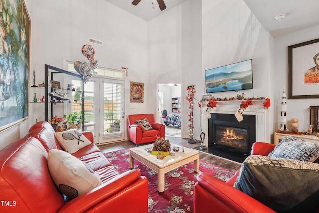 living room with a high ceiling, ceiling fan, and wood-type flooring