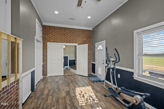 exercise area featuring ceiling fan, crown molding, dark wood-type flooring, and brick wall