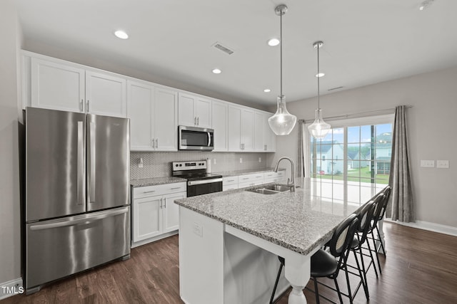 kitchen featuring a kitchen island with sink, hanging light fixtures, light stone countertops, appliances with stainless steel finishes, and white cabinetry