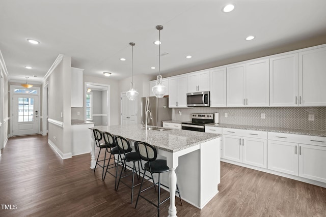 kitchen with dark wood-type flooring, a center island with sink, ornamental molding, white cabinetry, and stainless steel appliances