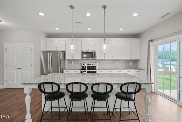 kitchen featuring dark hardwood / wood-style flooring, an island with sink, hanging light fixtures, and appliances with stainless steel finishes