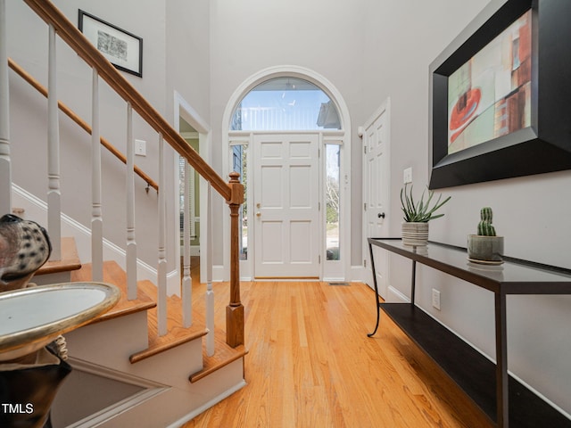 foyer with light wood-type flooring, stairway, and a towering ceiling