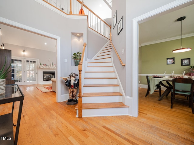 staircase with a towering ceiling, crown molding, wood finished floors, and a glass covered fireplace