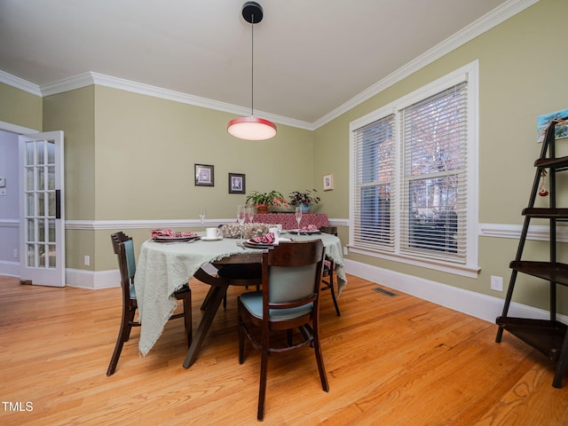 dining room featuring light wood finished floors, baseboards, visible vents, and ornamental molding