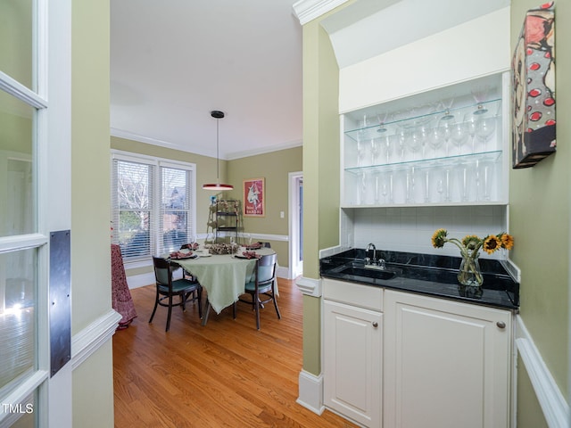 interior space featuring tasteful backsplash, light wood-style flooring, ornamental molding, white cabinetry, and a sink