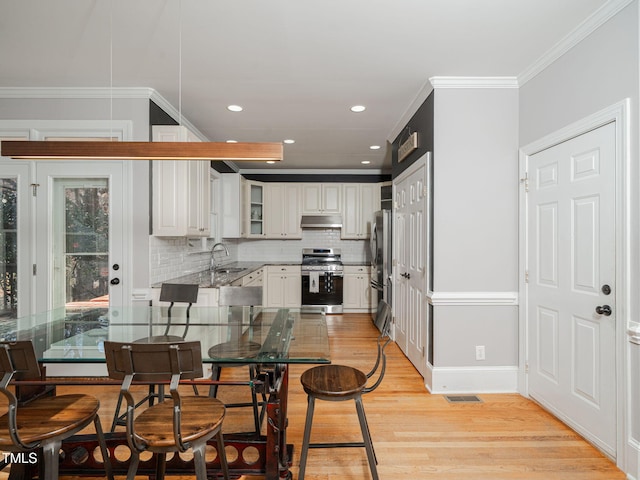 kitchen featuring ornamental molding, stainless steel appliances, light wood-type flooring, under cabinet range hood, and a sink