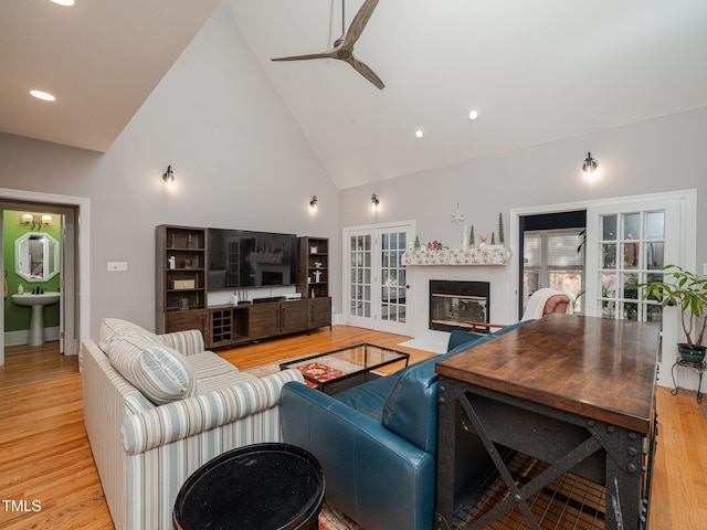 living room with a ceiling fan, a fireplace with flush hearth, french doors, light wood-style floors, and high vaulted ceiling