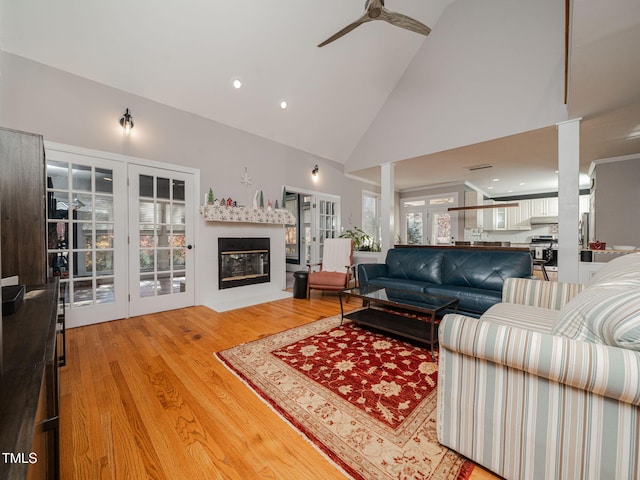 living room featuring a fireplace with flush hearth, ceiling fan, light wood-style flooring, and high vaulted ceiling