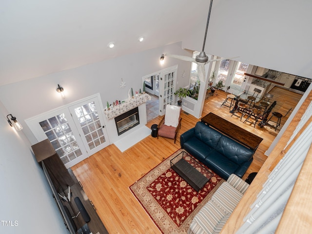 living area with french doors, a glass covered fireplace, ceiling fan, vaulted ceiling, and wood finished floors