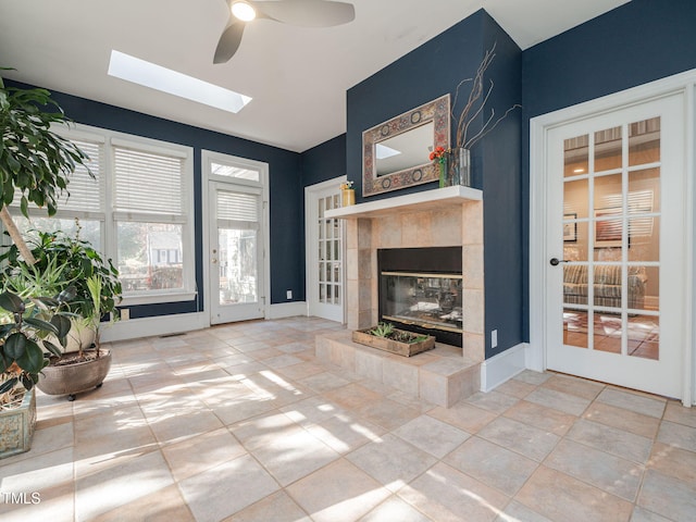 unfurnished living room featuring a skylight, a ceiling fan, baseboards, and a tiled fireplace