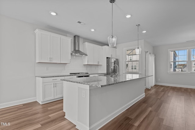 kitchen with a center island with sink, wall chimney exhaust hood, white cabinetry, and plenty of natural light