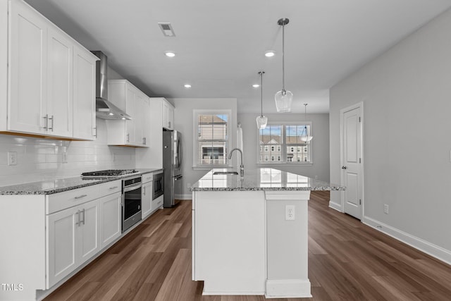 kitchen with white cabinetry, wall chimney range hood, stainless steel appliances, and hanging light fixtures