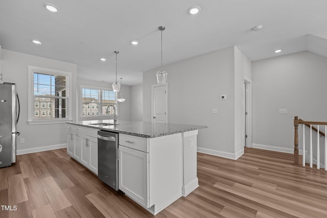 kitchen with appliances with stainless steel finishes, light wood-type flooring, pendant lighting, white cabinets, and an island with sink