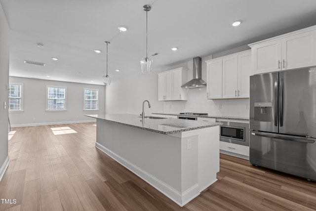 kitchen with pendant lighting, a center island with sink, white cabinets, wall chimney range hood, and appliances with stainless steel finishes