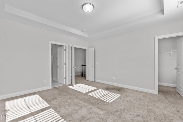 unfurnished bedroom featuring a tray ceiling, light carpet, and a closet