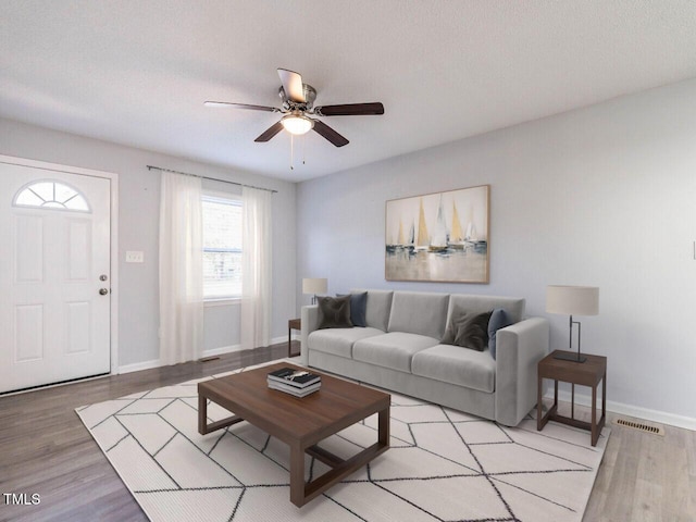 living room featuring ceiling fan, a textured ceiling, and light wood-type flooring