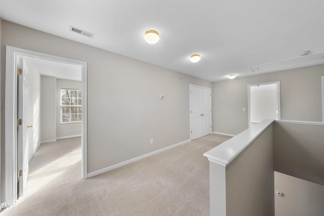 corridor with a textured ceiling and light carpet