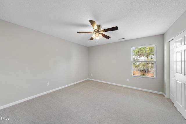 spare room with a textured ceiling, light colored carpet, and ceiling fan