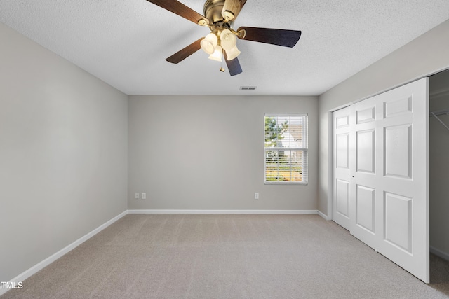 unfurnished bedroom featuring ceiling fan, a closet, light carpet, and a textured ceiling