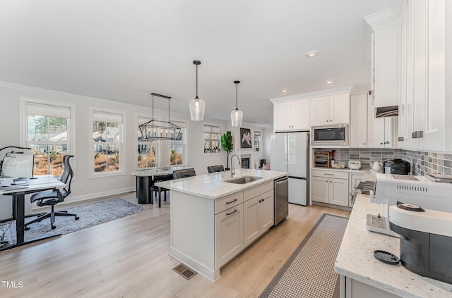 kitchen featuring stainless steel appliances, sink, decorative light fixtures, a center island with sink, and white cabinets