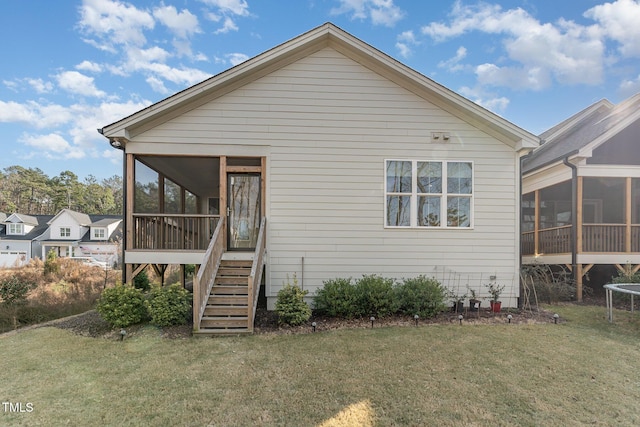 rear view of house with a sunroom, a trampoline, and a lawn