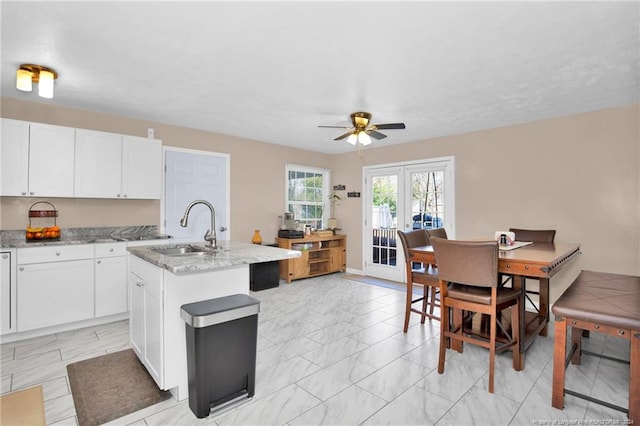 kitchen with white cabinets, sink, light stone countertops, and a kitchen island with sink