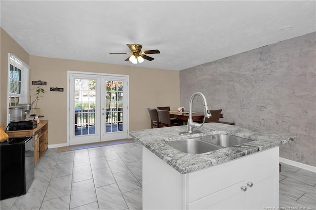 kitchen with french doors, light stone counters, ceiling fan, sink, and white cabinetry