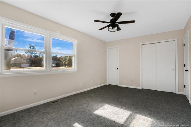 unfurnished bedroom with a closet, dark carpet, and ceiling fan