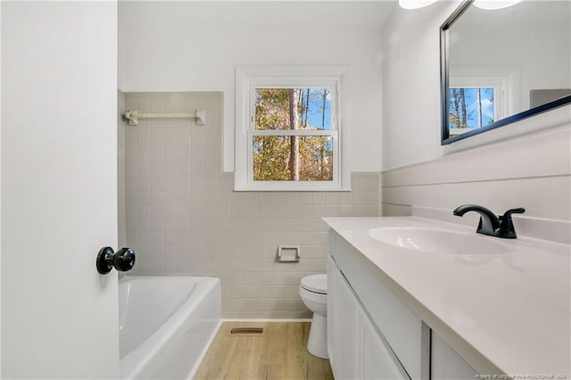 bathroom featuring a tub to relax in, vanity, tile walls, hardwood / wood-style floors, and toilet