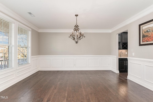 unfurnished dining area featuring a chandelier, dark hardwood / wood-style floors, crown molding, and sink