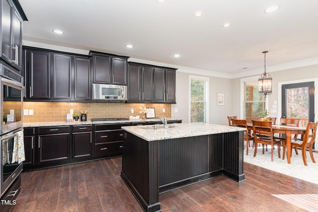 kitchen with a center island with sink, ornamental molding, decorative light fixtures, dark hardwood / wood-style flooring, and stainless steel appliances