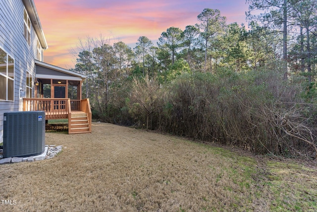 yard at dusk featuring central air condition unit, a wooden deck, and a sunroom