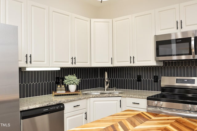 kitchen featuring backsplash, light stone counters, stainless steel appliances, sink, and white cabinetry