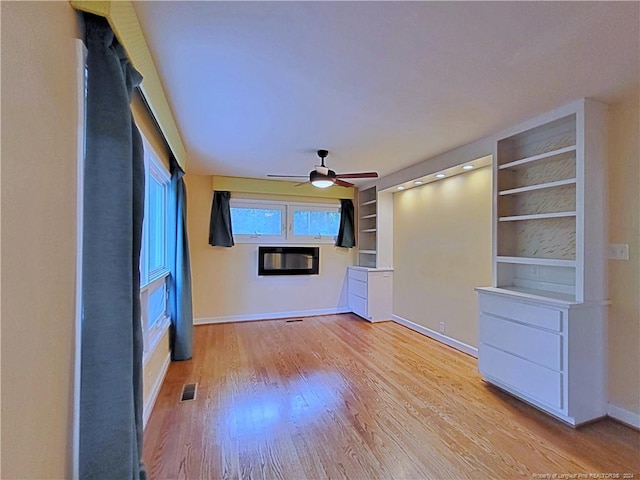 unfurnished living room featuring built in shelves, light hardwood / wood-style floors, and ceiling fan