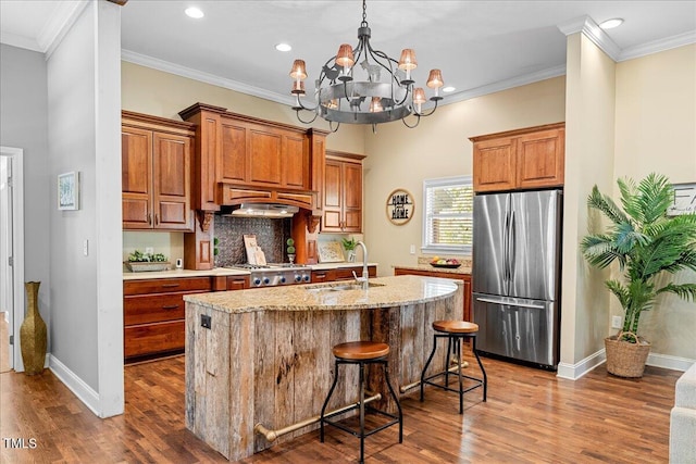 kitchen featuring a kitchen island with sink, a chandelier, stainless steel refrigerator, decorative backsplash, and sink