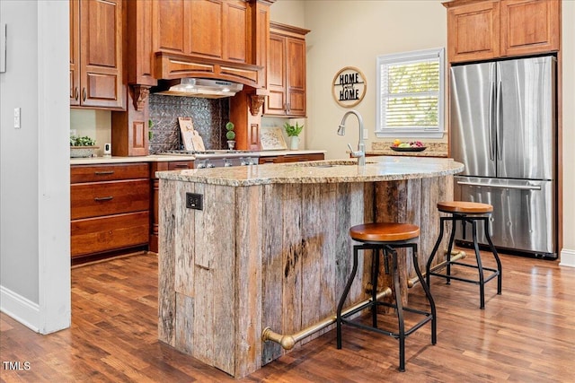 kitchen featuring appliances with stainless steel finishes, an island with sink, a breakfast bar, sink, and backsplash