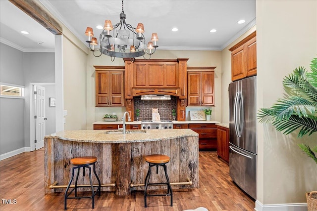 kitchen featuring sink, hanging light fixtures, stainless steel fridge, a center island with sink, and a breakfast bar