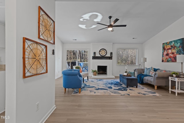 living room featuring plenty of natural light, a large fireplace, a ceiling fan, and wood finished floors