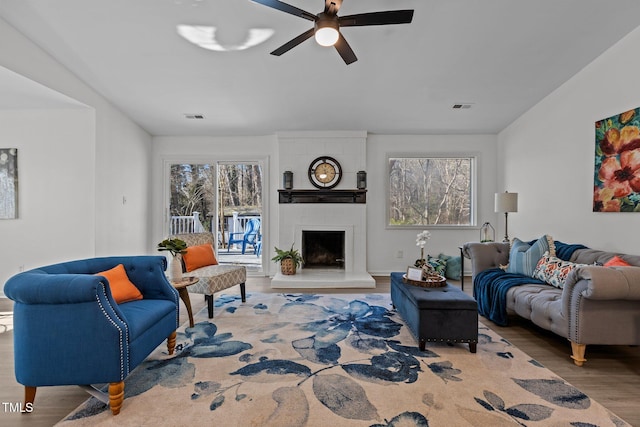 living room with a large fireplace, ceiling fan, and wood-type flooring