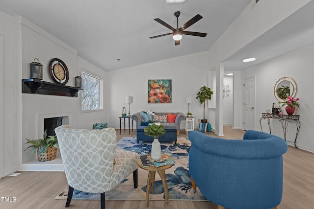 living room featuring light hardwood / wood-style floors, ceiling fan, vaulted ceiling, and a tiled fireplace