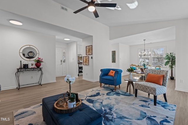 living room featuring ceiling fan with notable chandelier, lofted ceiling, and light wood-type flooring