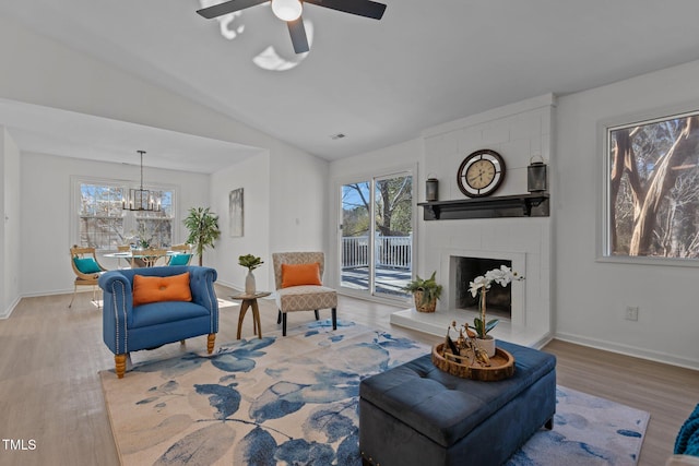 living room with ceiling fan with notable chandelier, a fireplace, light hardwood / wood-style floors, and lofted ceiling