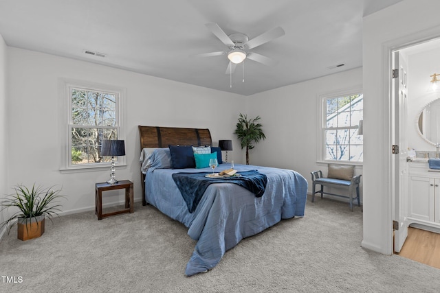 bedroom with multiple windows, connected bathroom, ceiling fan, and light colored carpet