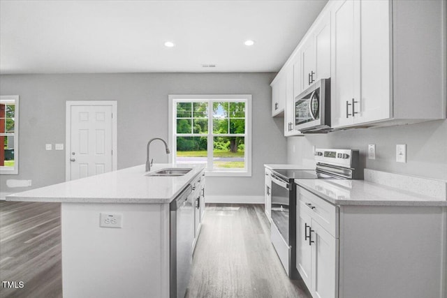 kitchen with sink, dark wood-type flooring, stainless steel appliances, a center island with sink, and white cabinets