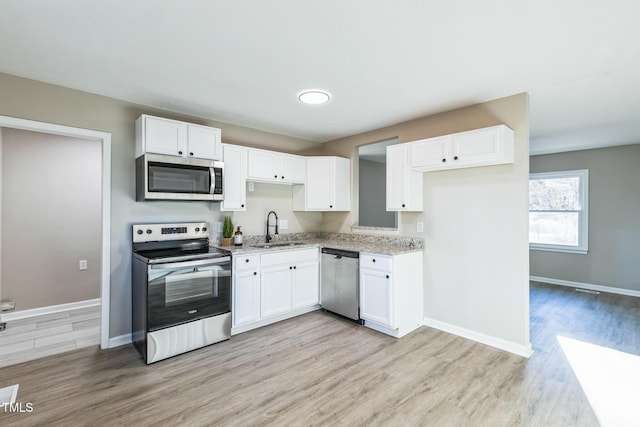 kitchen with white cabinets, sink, light hardwood / wood-style floors, light stone counters, and stainless steel appliances